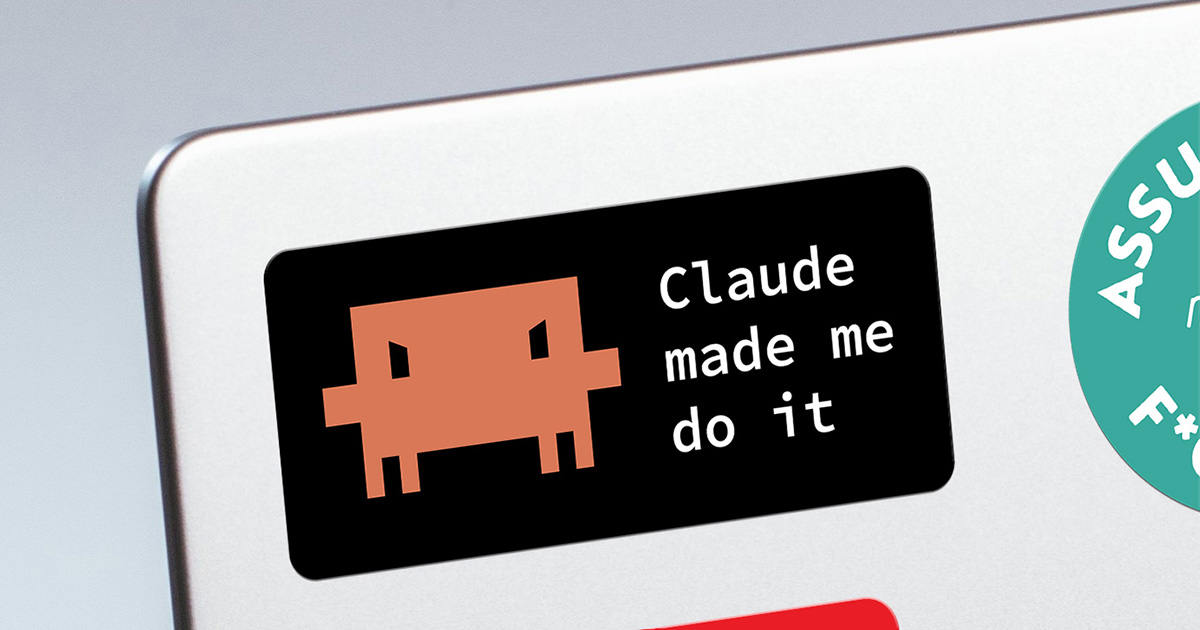 A black rectangular sticker on a silver laptop lid showing a mischievous looking pixel-art Claude logo next to the monospaced text "Claude made me do it". A teal round sticker is partly visible at the right.